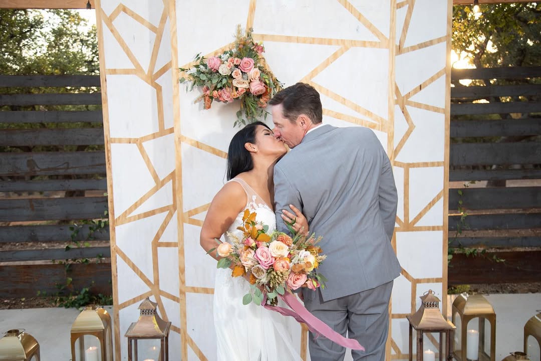 Bride and groom first kiss at Prima Vista ceremony backdrop Wimberley TX